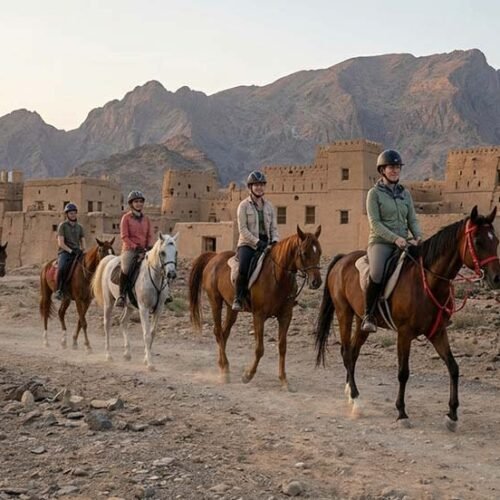 Riders on horseback with a guide below the old houses of Al Hamra