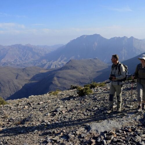 Two hikers on a rocky ridge with mountains behind