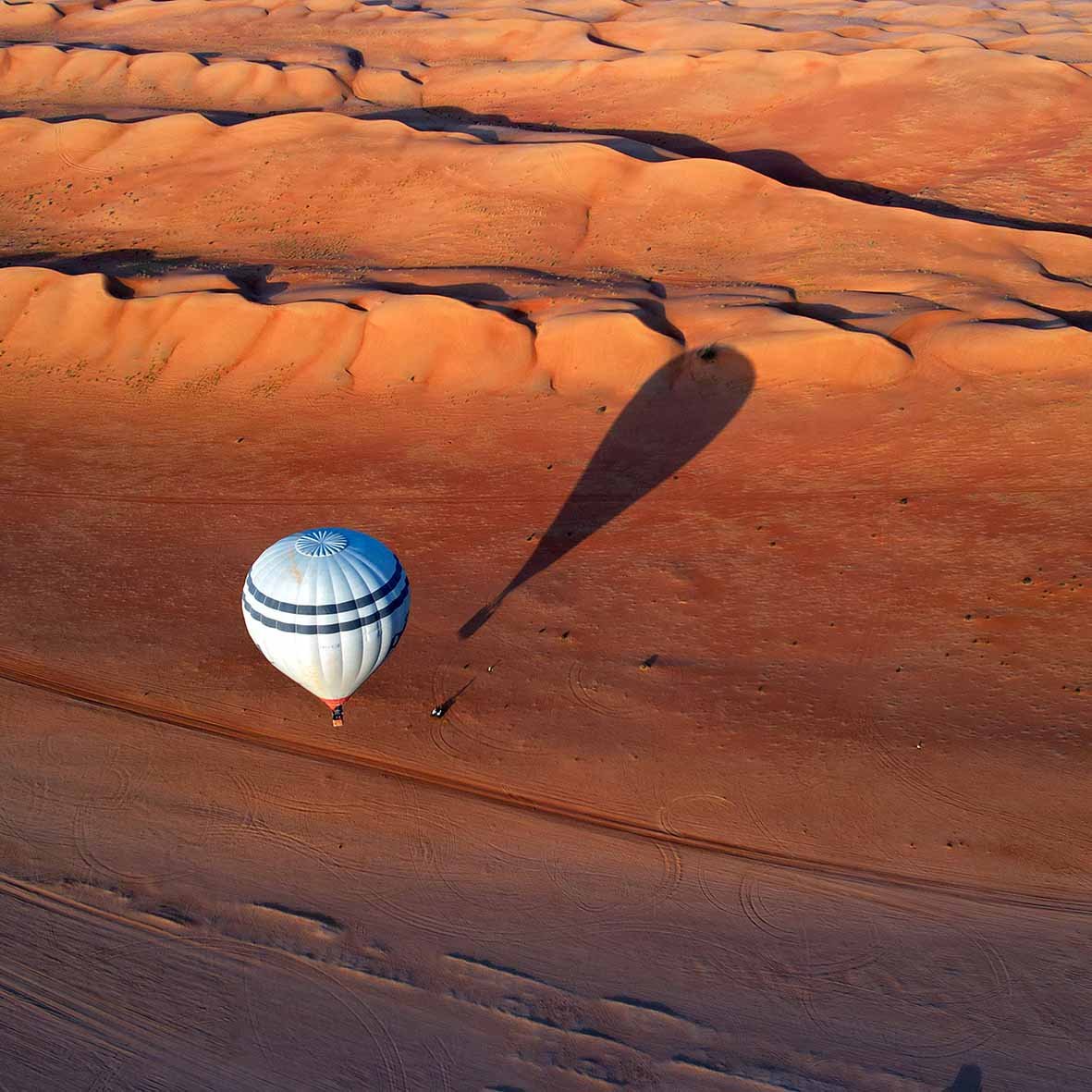 A hot-air balloon and its shadow over orange dunes