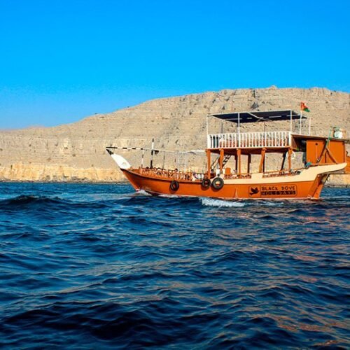 A dhow cruising between the cliffs of a Musandam fjord