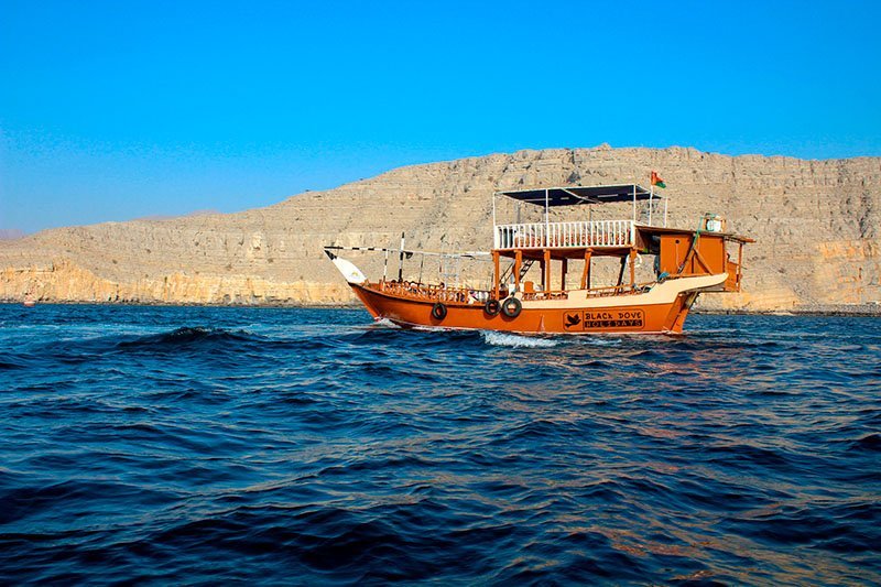 A dhow cruising between the cliffs of a Musandam fjord