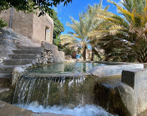 Water flowing from a falaj into a stone basin in Misfat