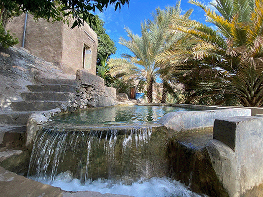 Water flowing from a falaj into a stone basin in Misfat