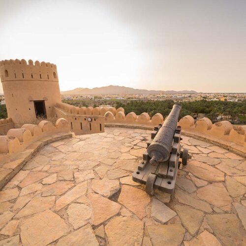 A cannon on the stone terrace of Nakhal Fort, with a watchtower