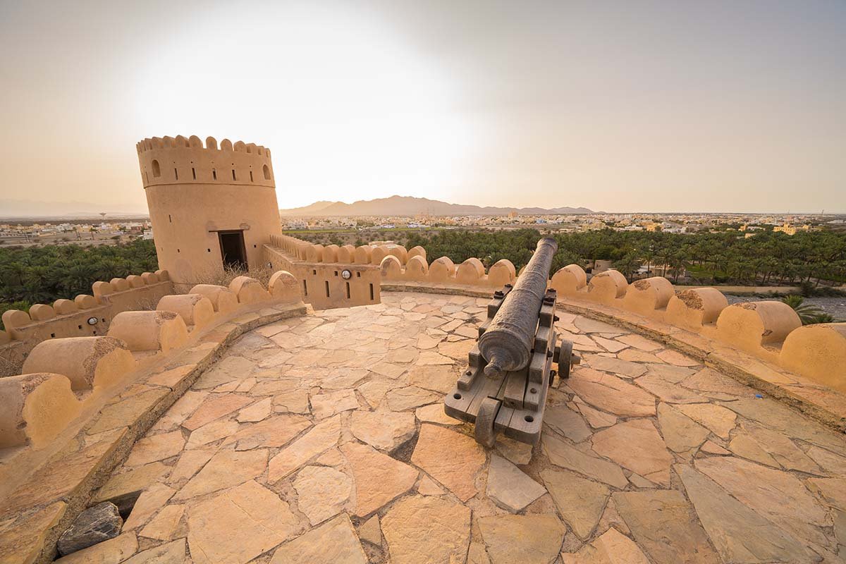 A cannon on the stone terrace of Nakhal Fort, with a watchtower