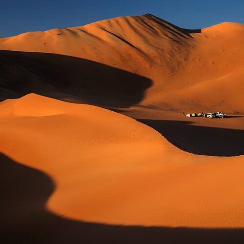 Tall orange dunes in the Empty Quarter, with a camp far below