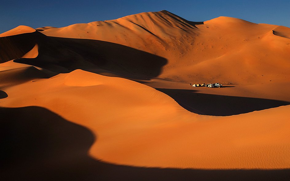 Tall orange dunes in the Empty Quarter, with a camp far below