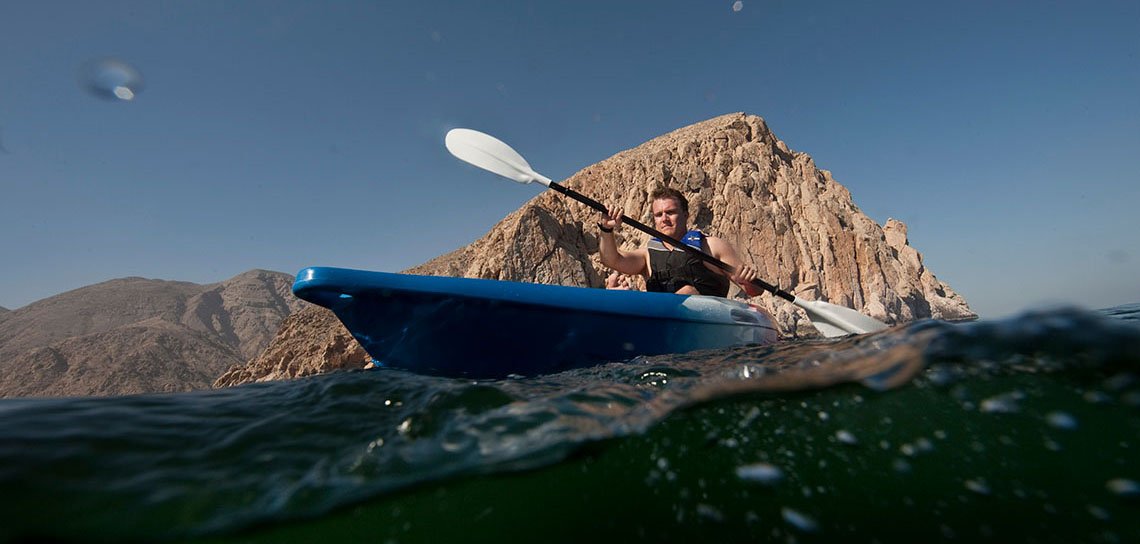 A kayaker paddling below a rocky headland in Musandam