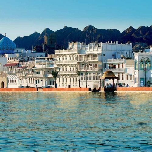 Houses and a mosque along the Mutrah Corniche, with mountains behind