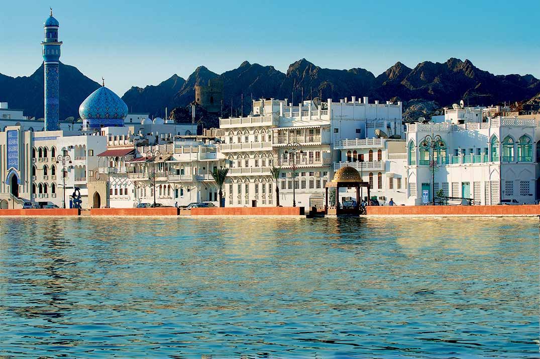 Houses and a mosque along the Mutrah Corniche, with mountains behind
