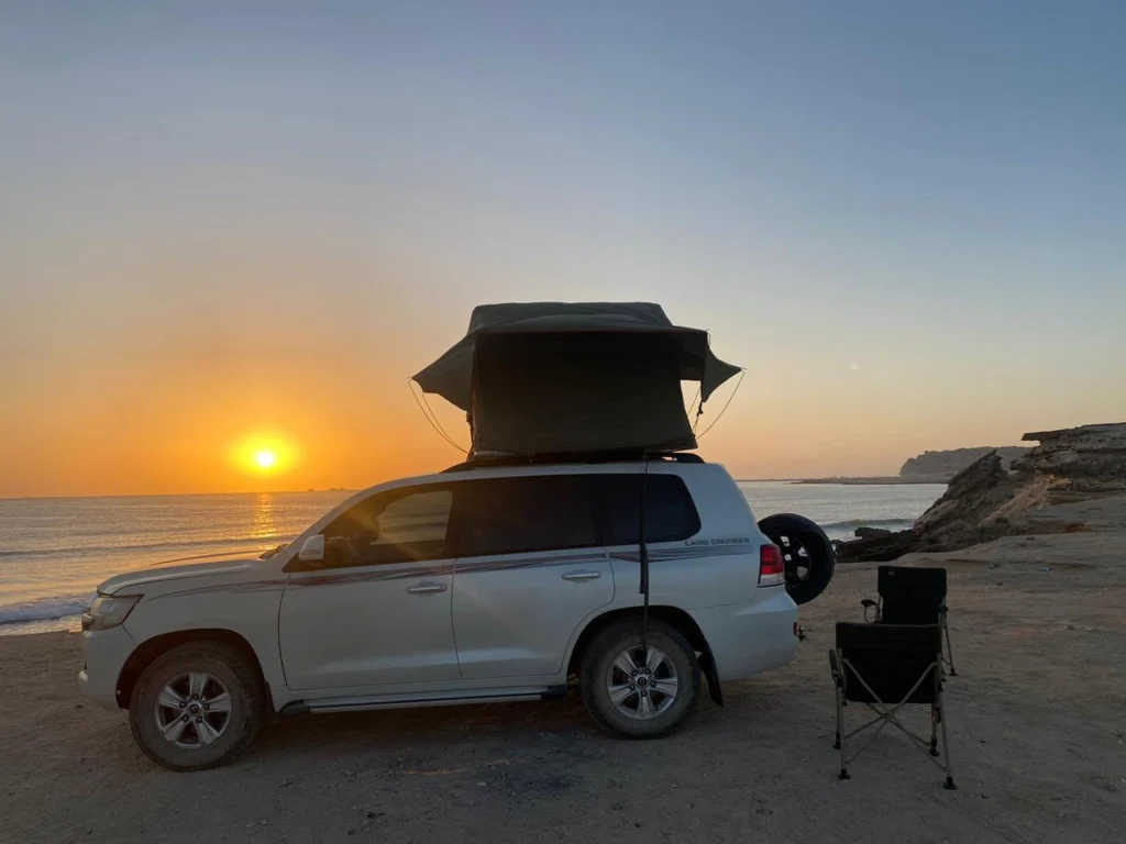 A white 4x4 with its rooftop tent open on a beach as the sun sets over the sea