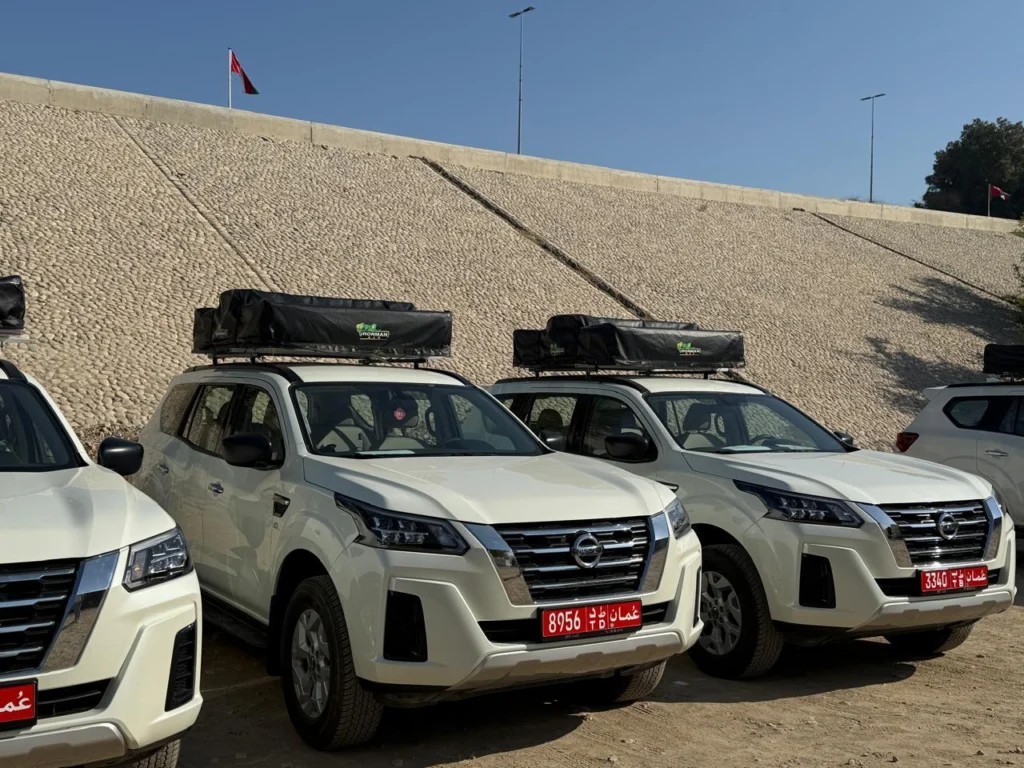A row of white fleet 4x4s with roof racks lined up on a dirt lot