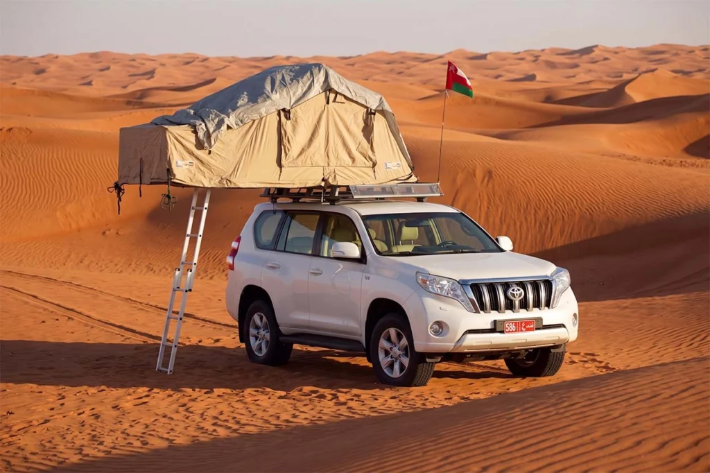 White 4x4 with a rooftop tent on a red sand dune in the Wahiba Sands