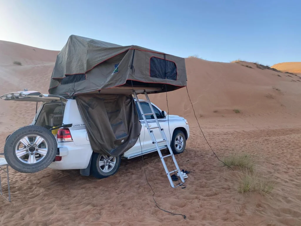 A white Land Cruiser with its rooftop tent and ladder set up among desert dunes