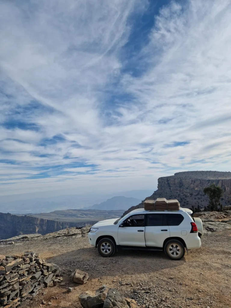 A white 4x4 parked on a rocky mountain viewpoint under a sky of high cloud