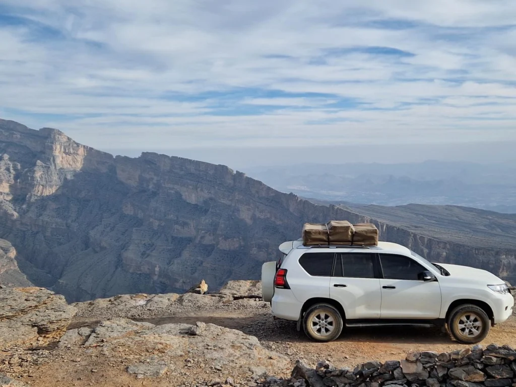 A white 4x4 parked at the edge of a deep mountain canyon under a wide sky