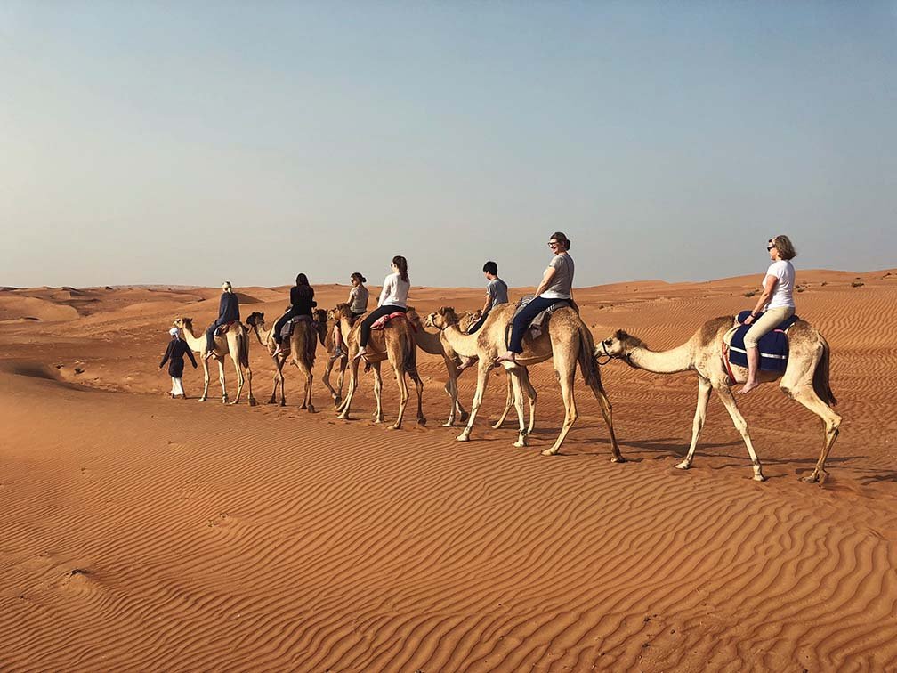 Riders on camels crossing the dunes of the Wahiba Sands