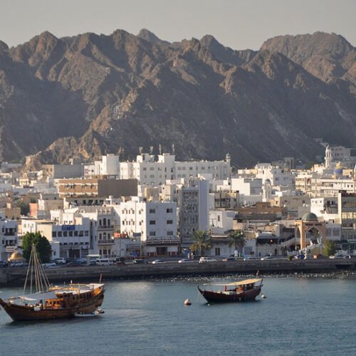 Mutrah waterfront: white buildings below bare mountains, with dhows in the harbour