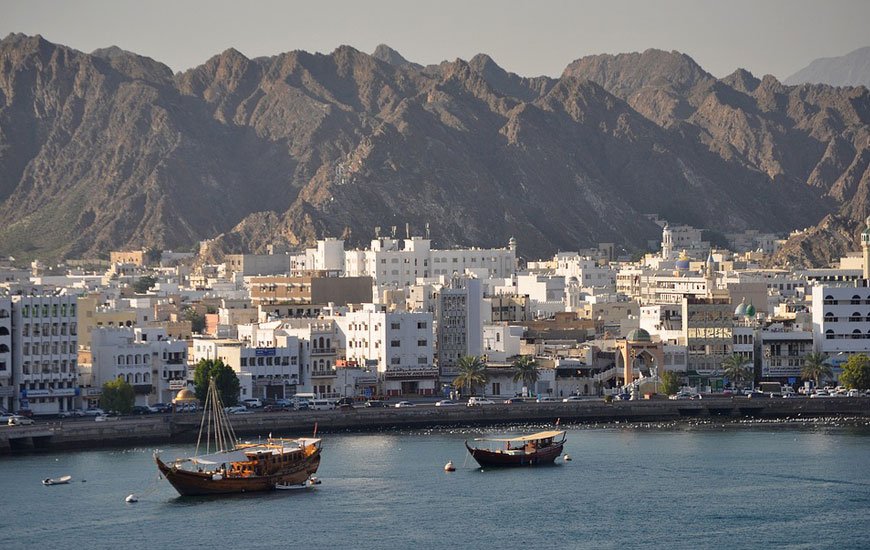 Mutrah waterfront: white buildings below bare mountains, with dhows in the harbour
