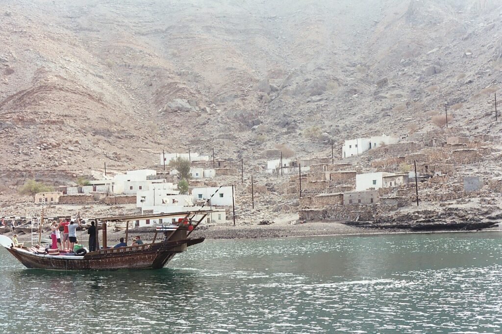 White houses of a fishing village at the foot of bare mountains, with a dhow on the water in front