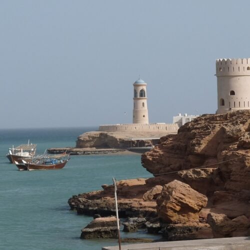 Watchtowers and a lighthouse on a rocky shore, with dhows at anchor