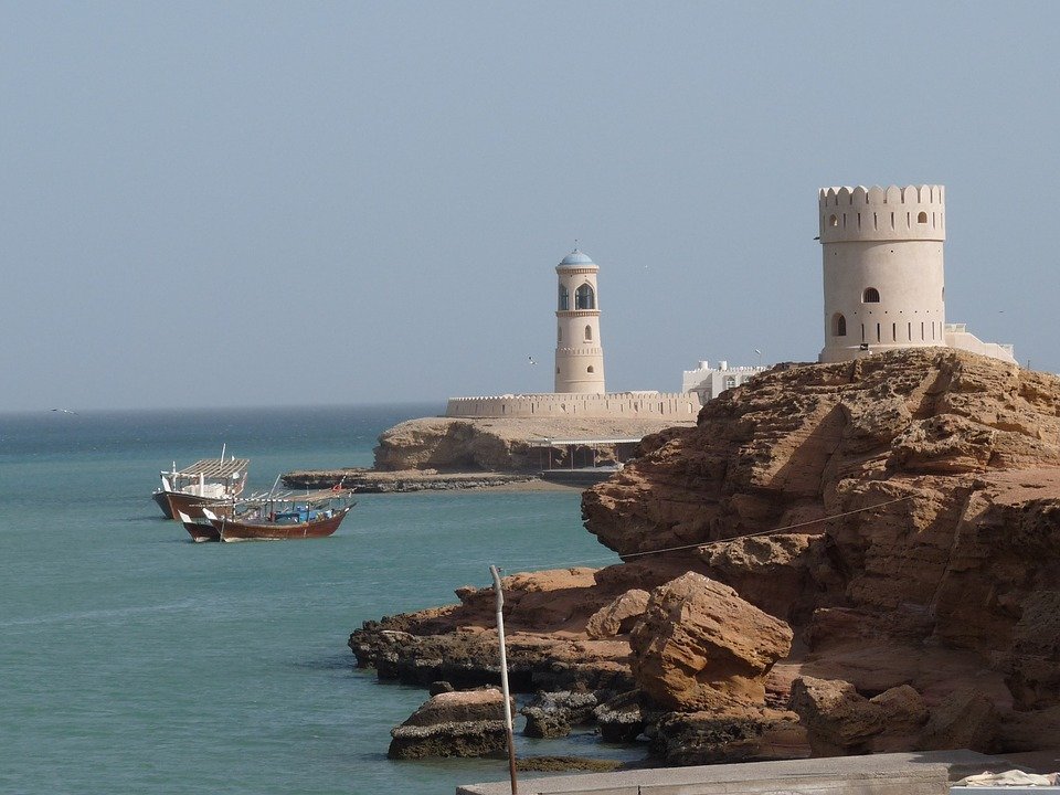 Watchtowers and a lighthouse on a rocky shore, with dhows at anchor