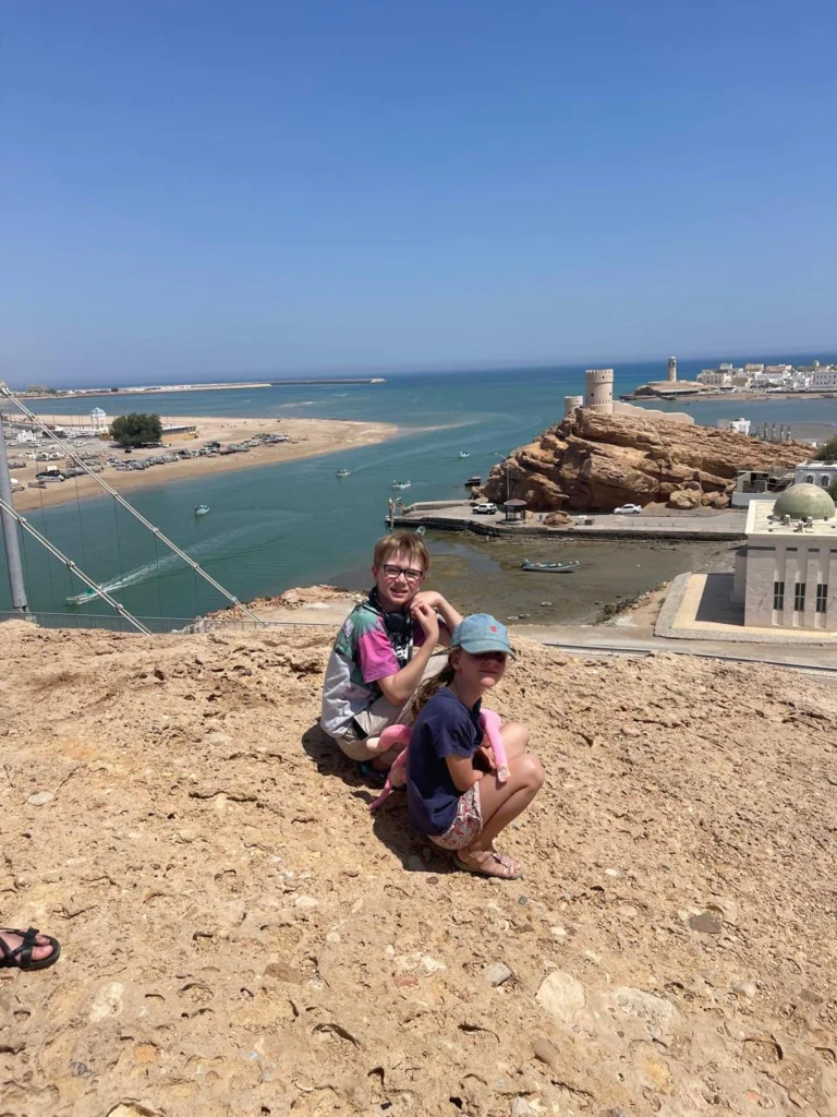 Two children sitting on a hill above a coastal lagoon and old watchtower