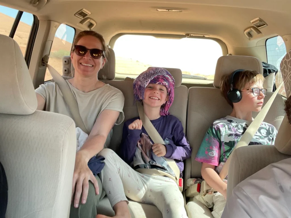 A mother and two children smiling in the back of a 4x4 in the desert