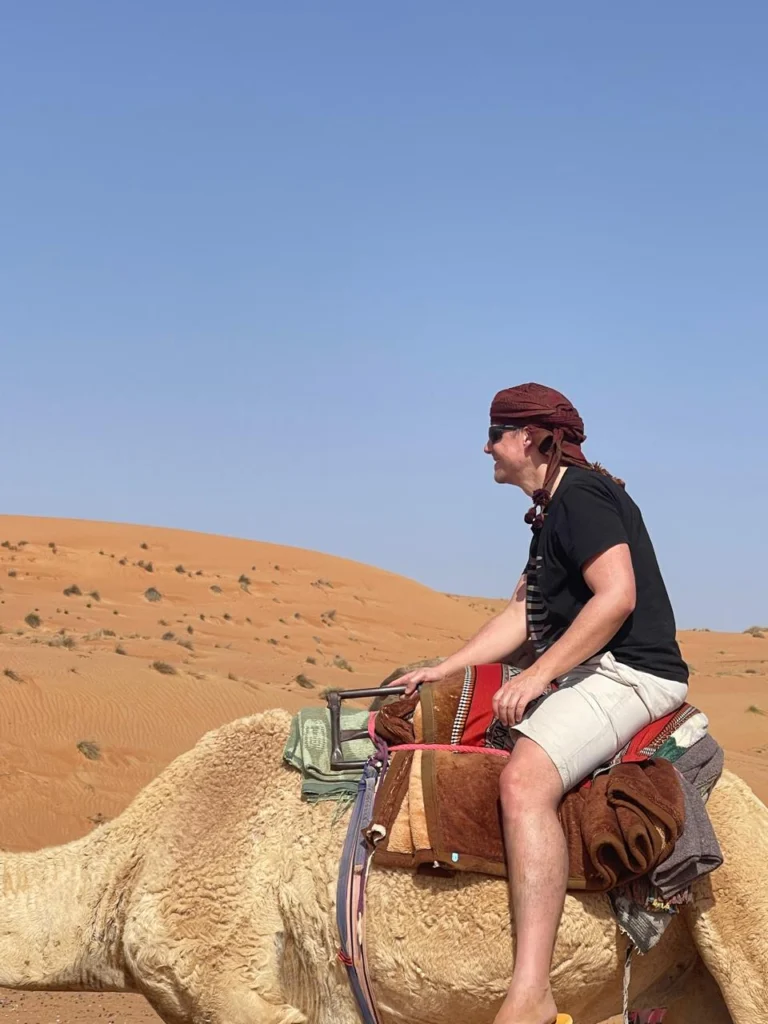 A guest in a head scarf riding a camel across sand dunes