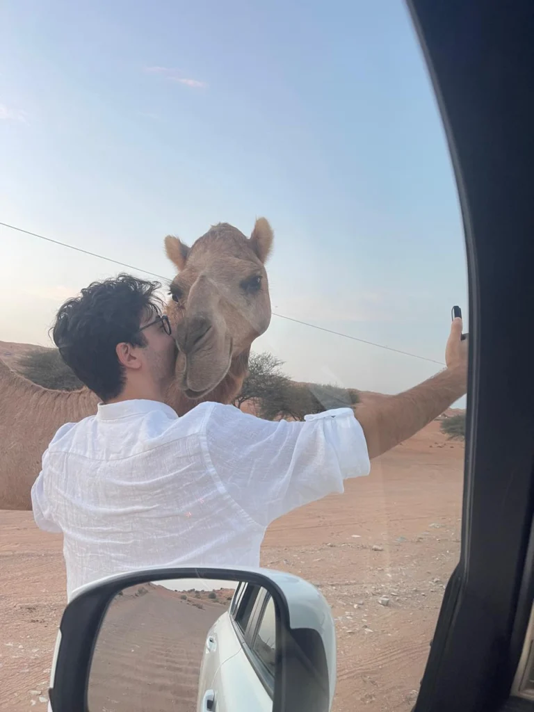 A guest standing by a 4x4 as a camel nuzzles close
