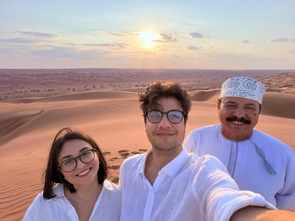 Two guests and their guide taking a selfie on a dune at sunset