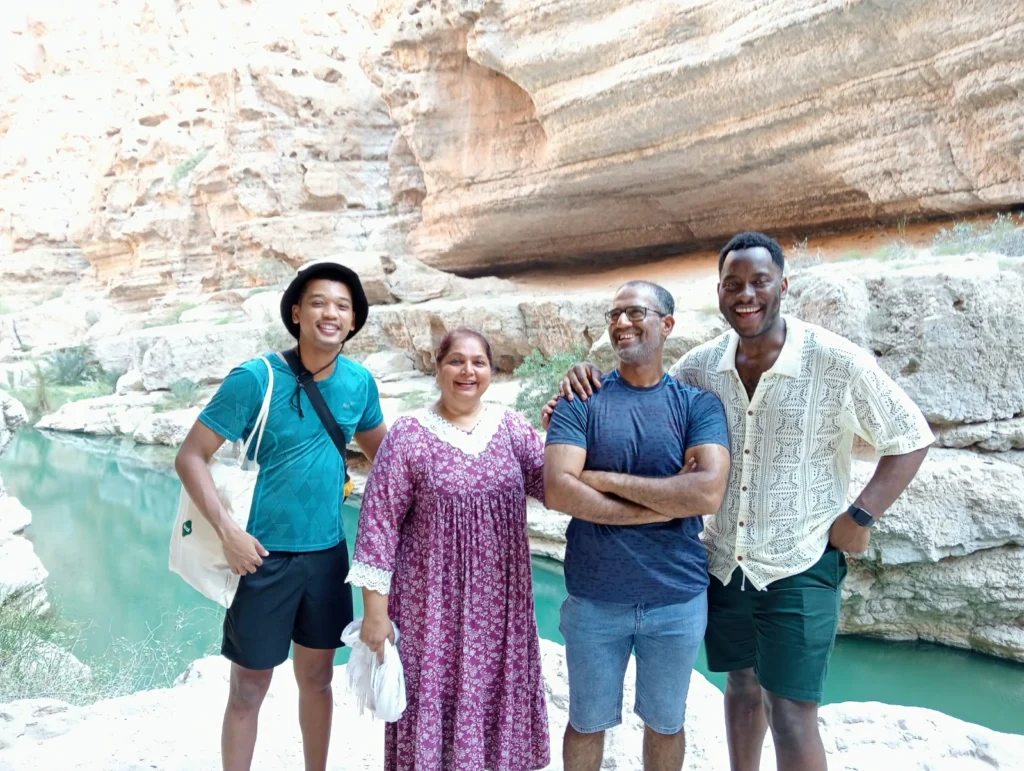 Four guests smiling beside a turquoise wadi pool
