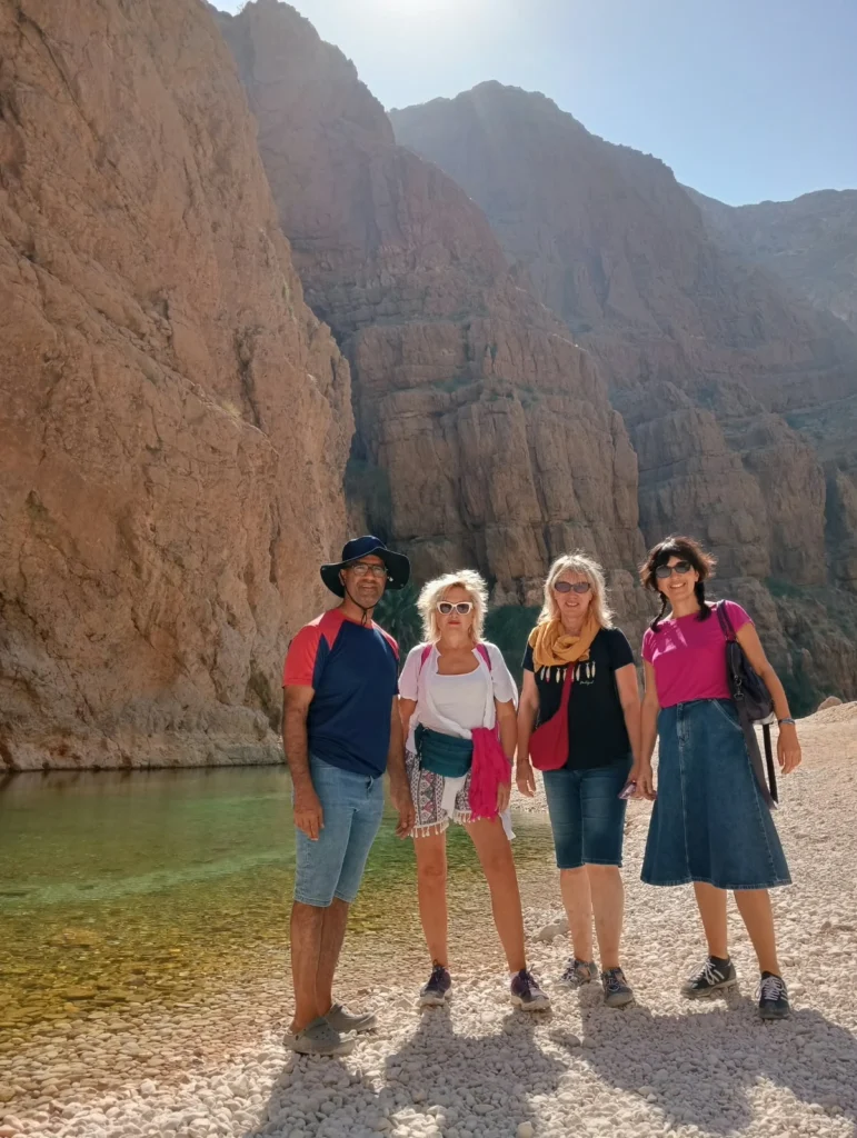 Four guests standing at a pool beneath tall wadi canyon walls