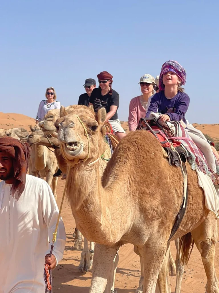 Guests including a child riding camels across the desert