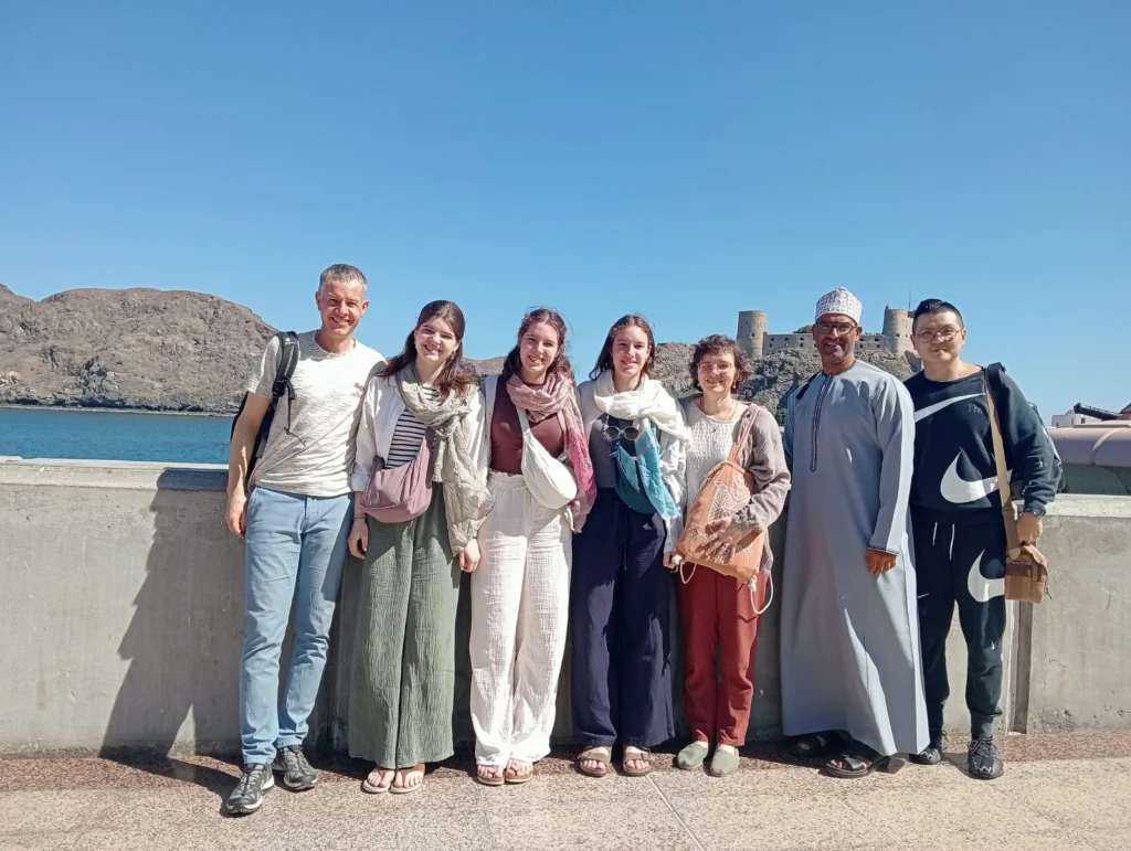 Guests and their guide lined up at a seafront wall with a fort behind