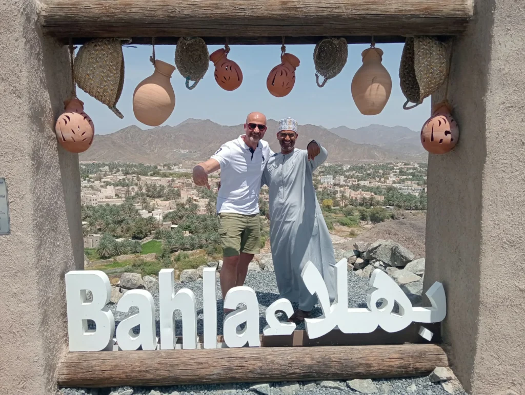 A guest and an Omani guide posing in a frame with the Bahla town sign