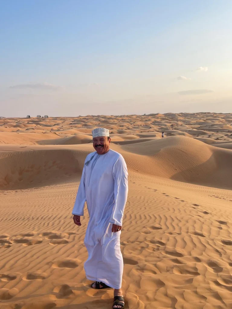 An Omani guide walking across rippled desert sand dunes