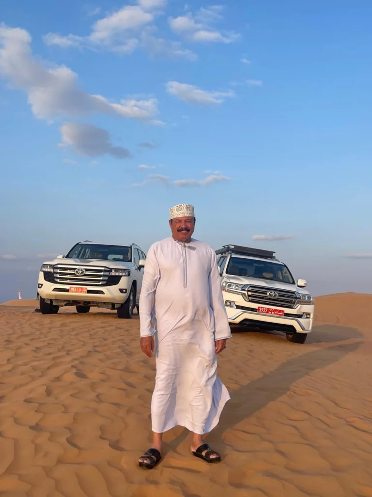An Omani guide standing between two 4x4 vehicles on the sand dunes