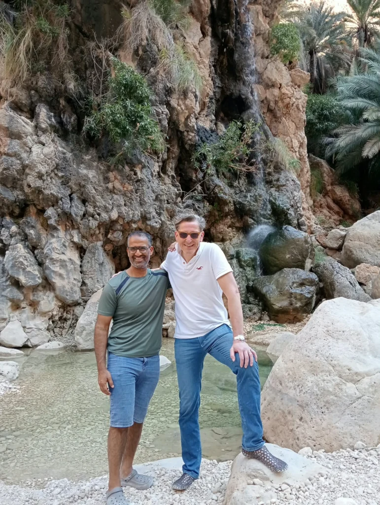Two guests posing on rocks beside a green wadi pool